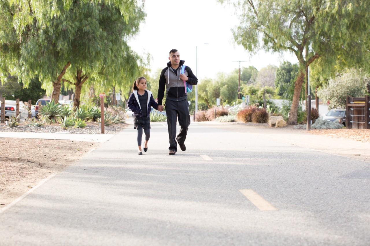 父亲和女儿在惠蒂尔绿道散步，这是一条4.5英里长的休闲通勤自行车道和步行道。Whittier, California. 2016.  Greenway Trail. Many familes use the trail system to get to school. Signs of Progress.