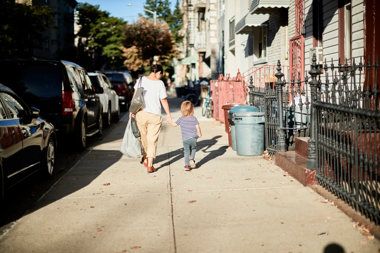 一位母亲牵着小女儿的手走在城市的人行道上。