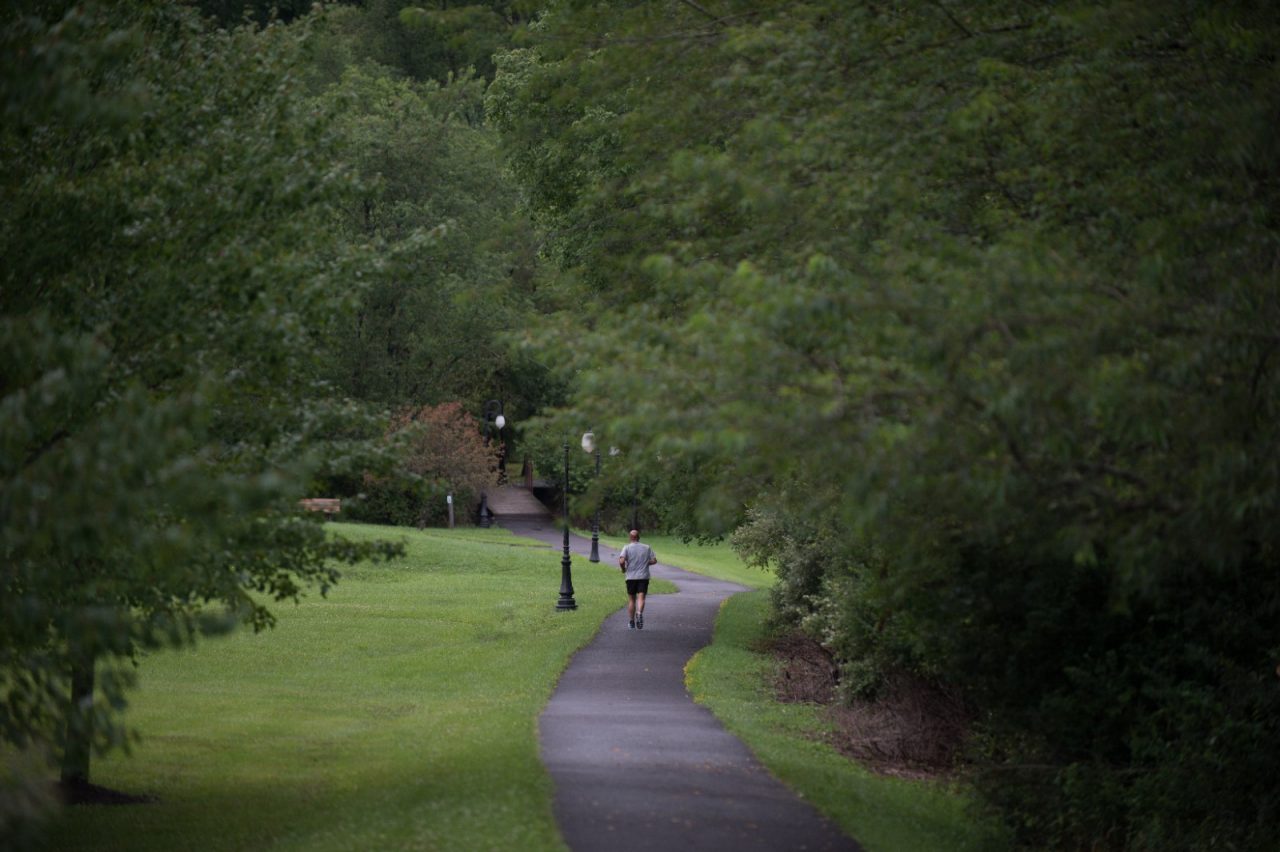一个男人在一条小路上奔跑，小路两边都是杂草丛生的树木。